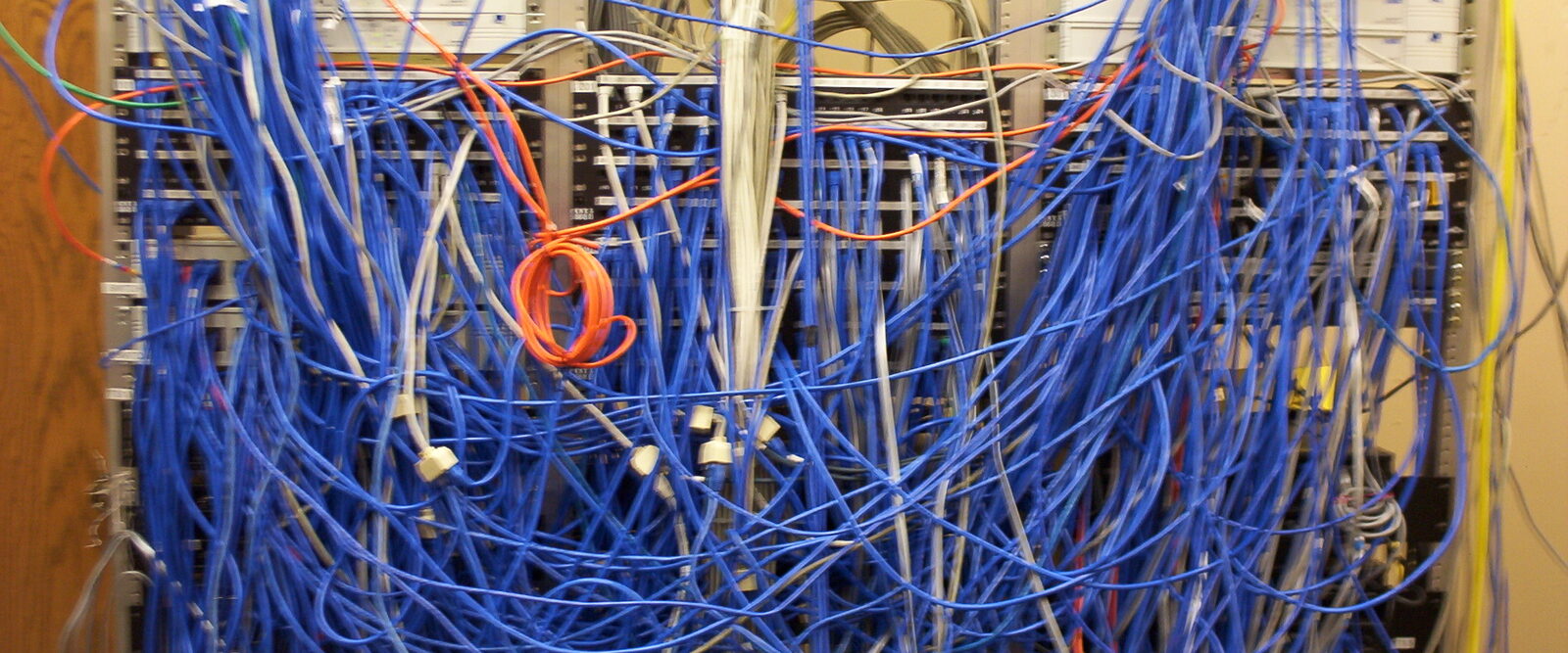 A network cabinet with hundreds of blue cables tangled across the front of the racks