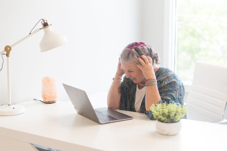 A business owner at her laptop with her head in her hands, stuck with technology that is not working for her