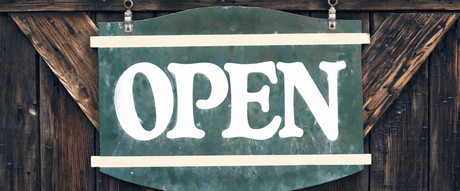 A painted OPEN sign hanging on a wooden shop door