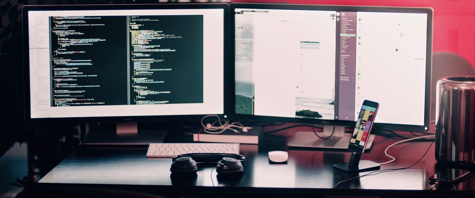 A developer's desk with code on two screens and a phone on a stand